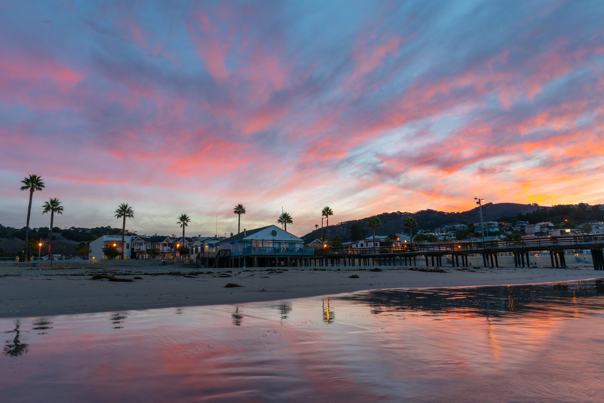 Pink and blue clouds over the beach houses, palm trees and pier along Avila Beach