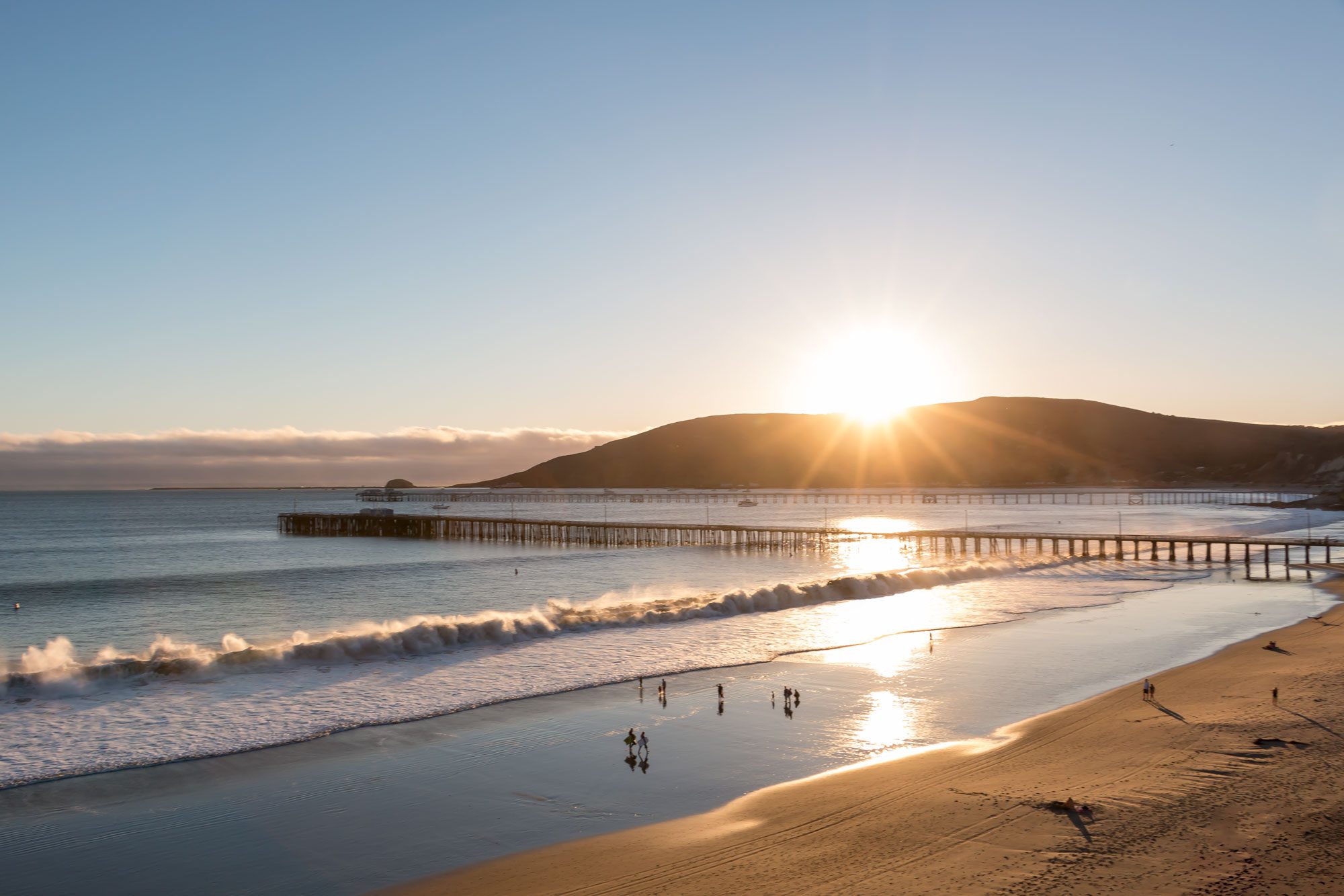 The sun setting behind Port San Luis with Avila Pier and Harford Pier stretching into the bay
