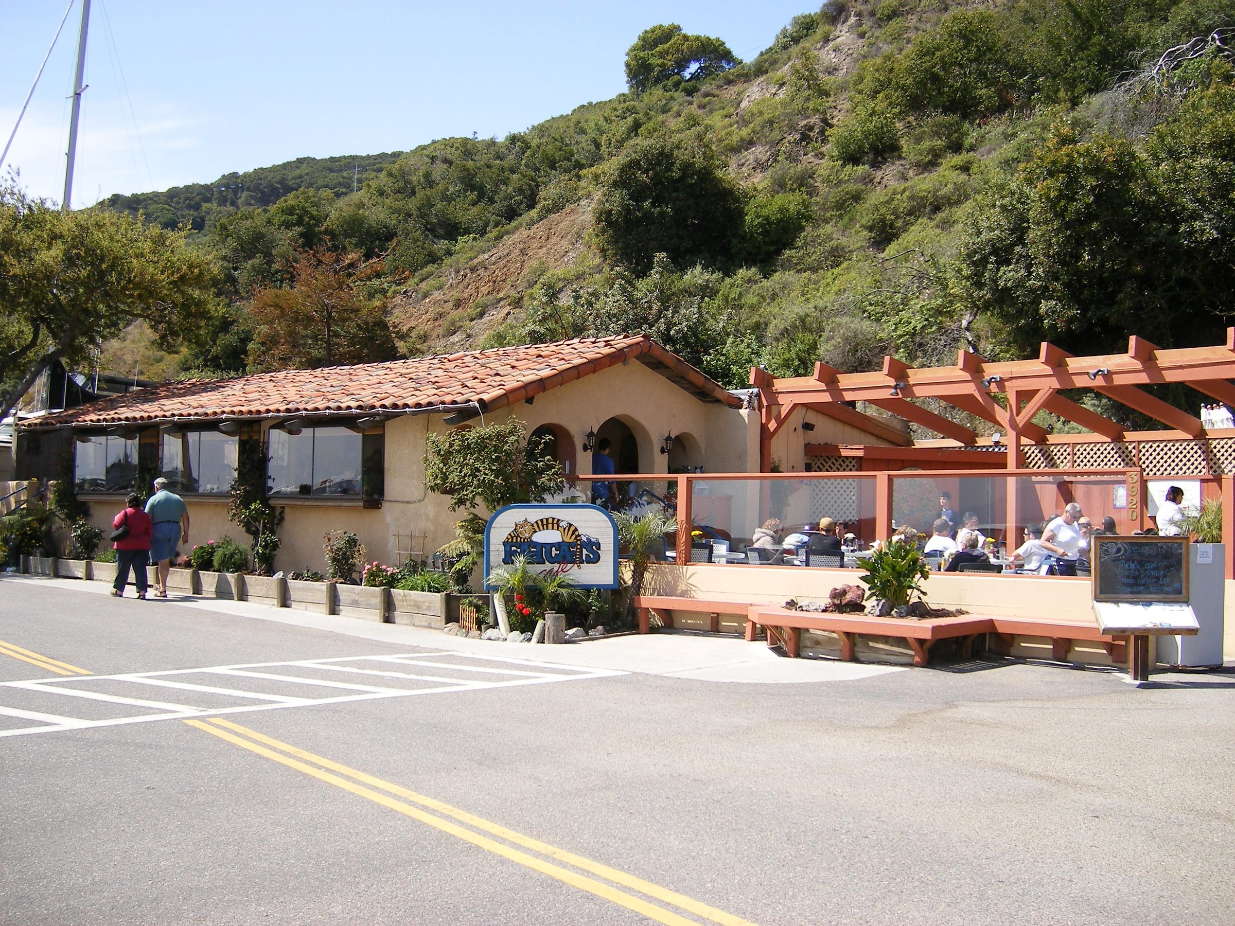 Fat Cats Cafe at the base of Harford Pier, with diners on the patio below the green hillside