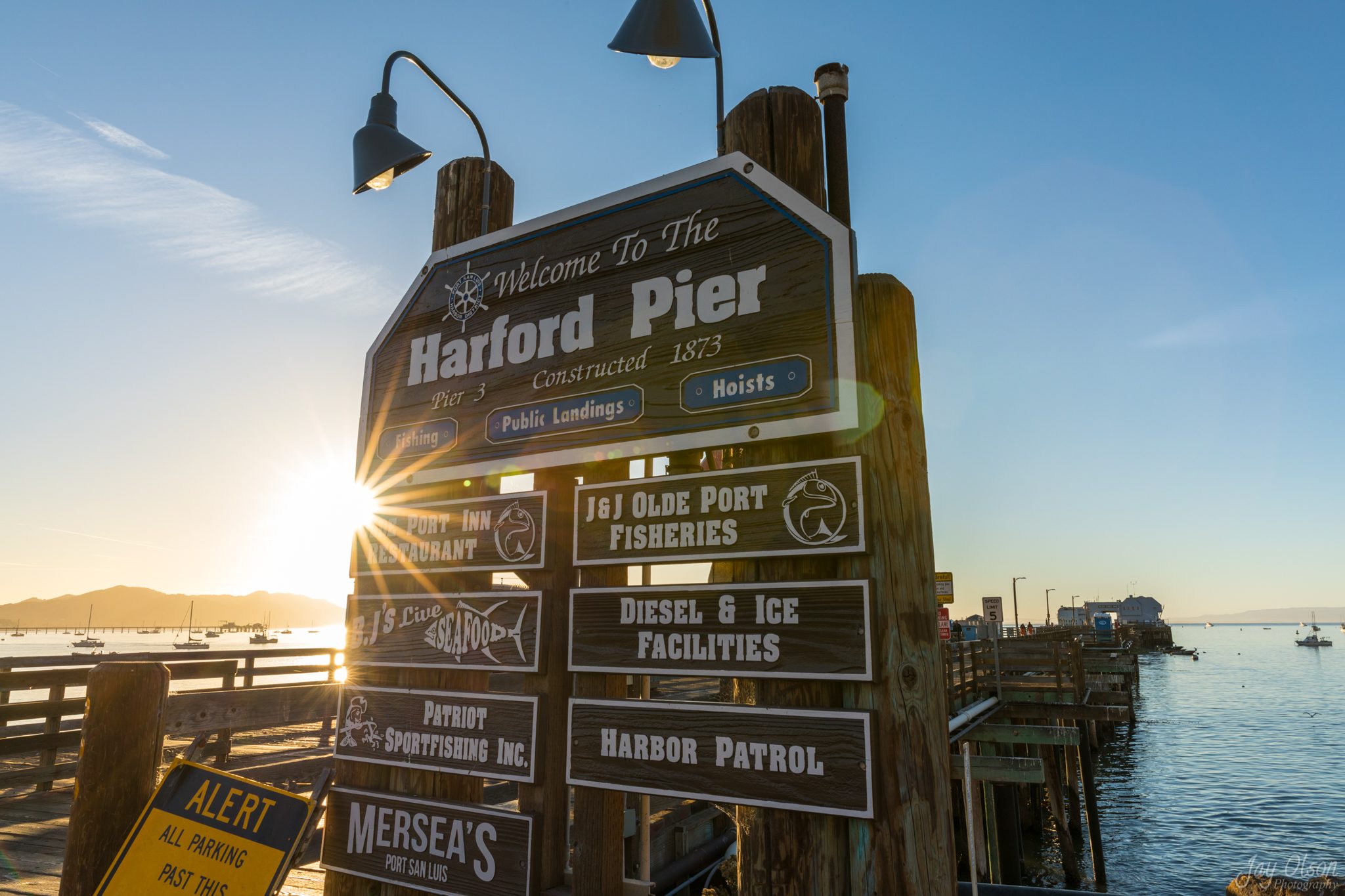 The Welcome to Harford Pier sign listing the fish markets, restaurants and sportfishing, with the sun bursting behind it