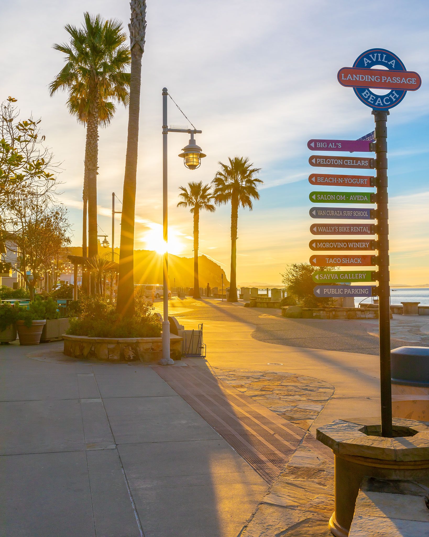 The Avila Beach Landing Passage sign pointing to shops and restaurants at sunrise