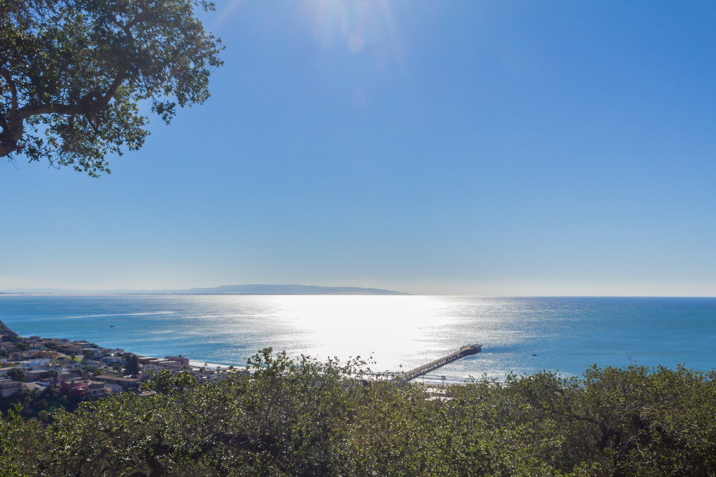 Sun glittering on San Luis Bay and Avila Pier, framed by oaks on the hillside above town