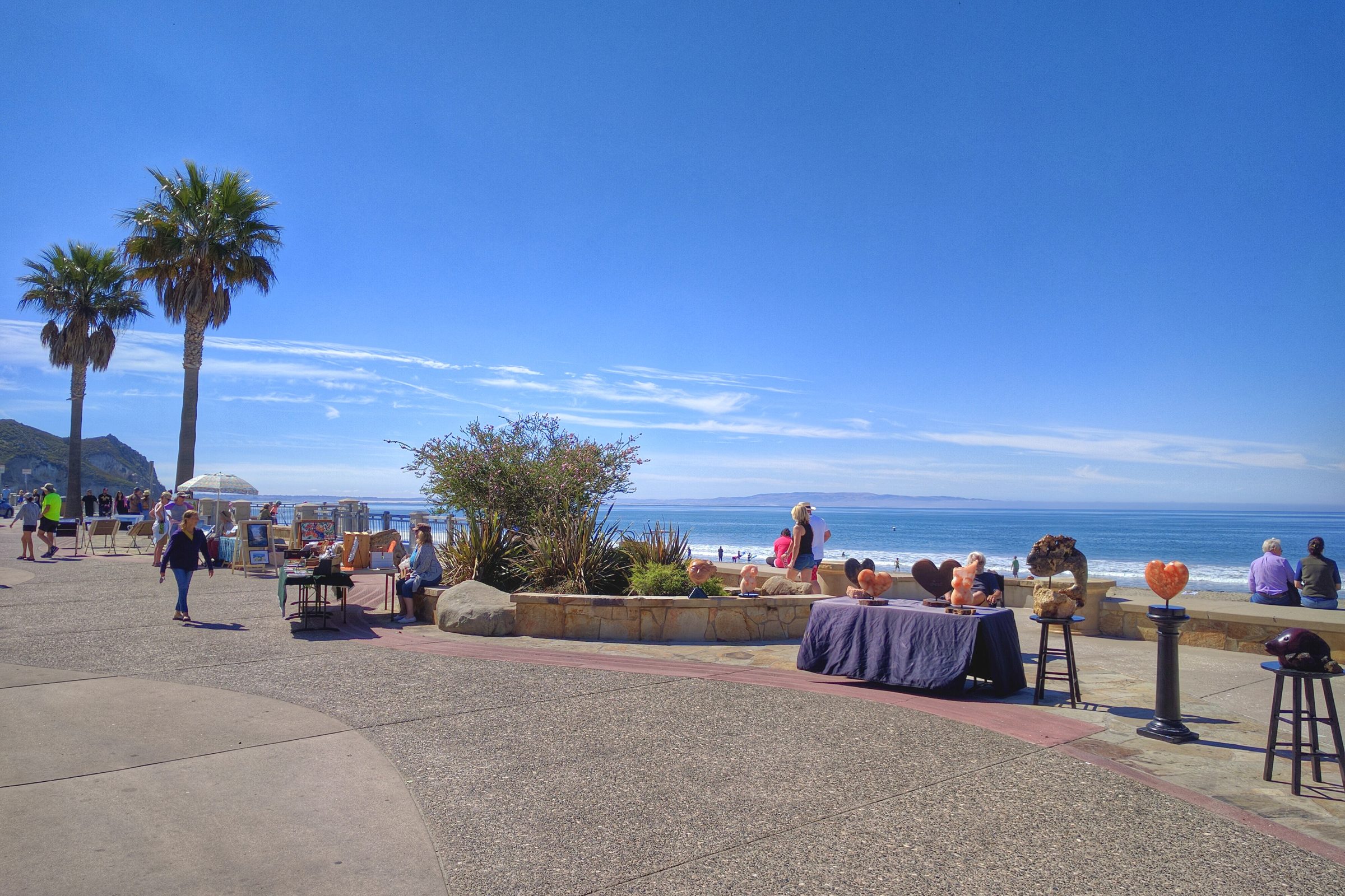 Artists selling paintings and sculpture along the Avila Beach promenade on a sunny day