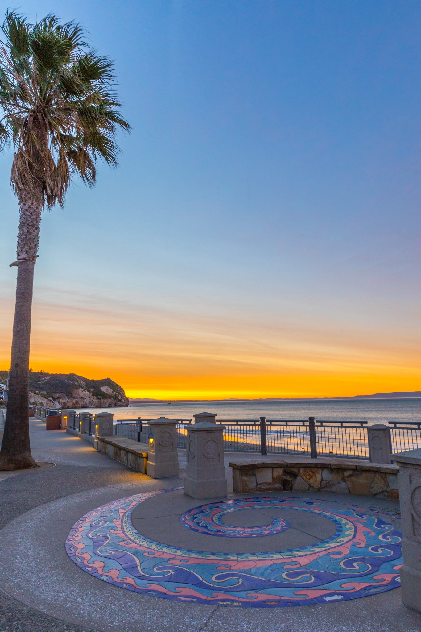 The swirling tile mosaic and a palm tree on the Avila Beach promenade at dawn