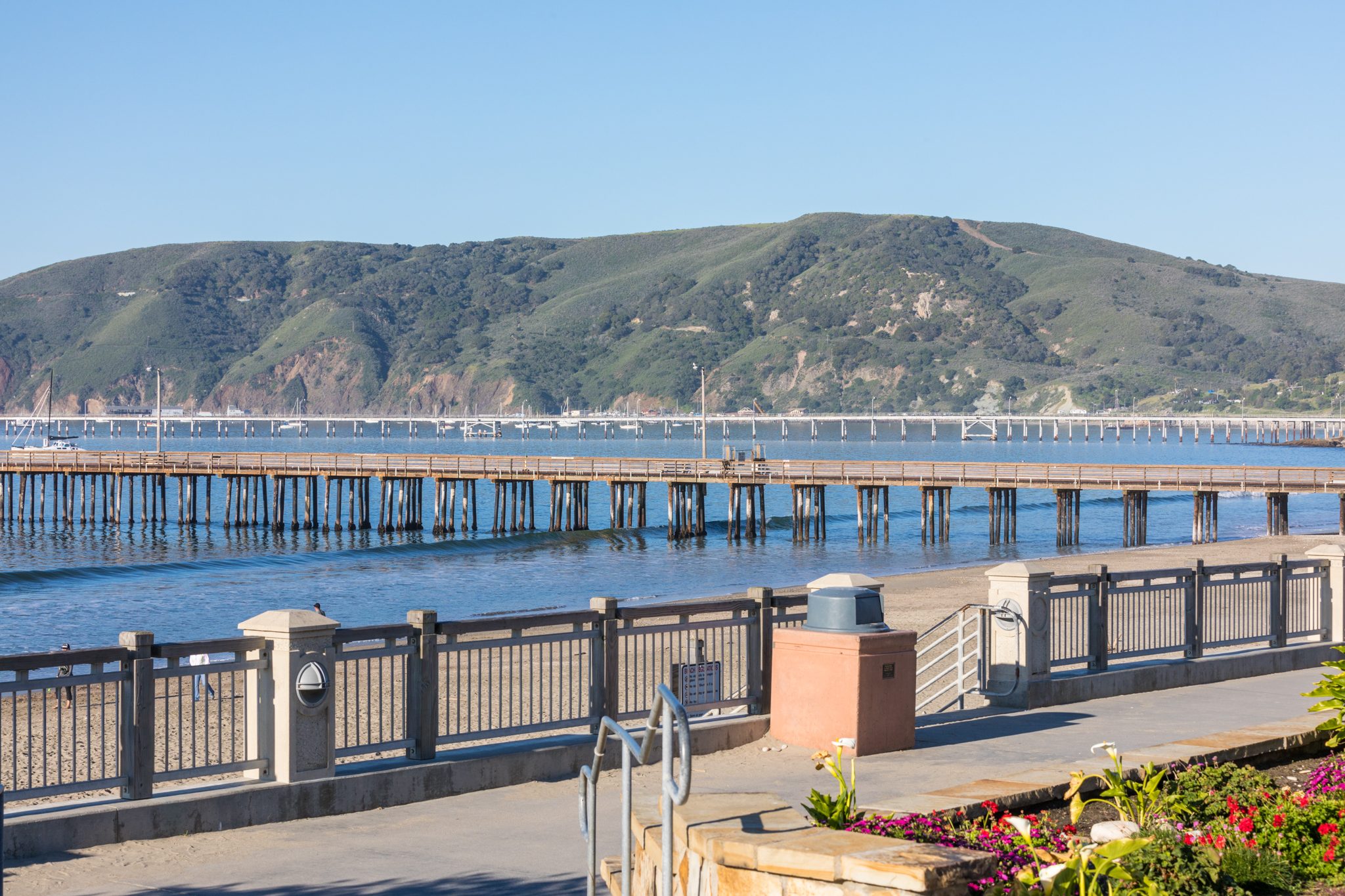 The promenade railing above the beach, with Avila Pier, Cal Poly Pier and green spring hills behind
