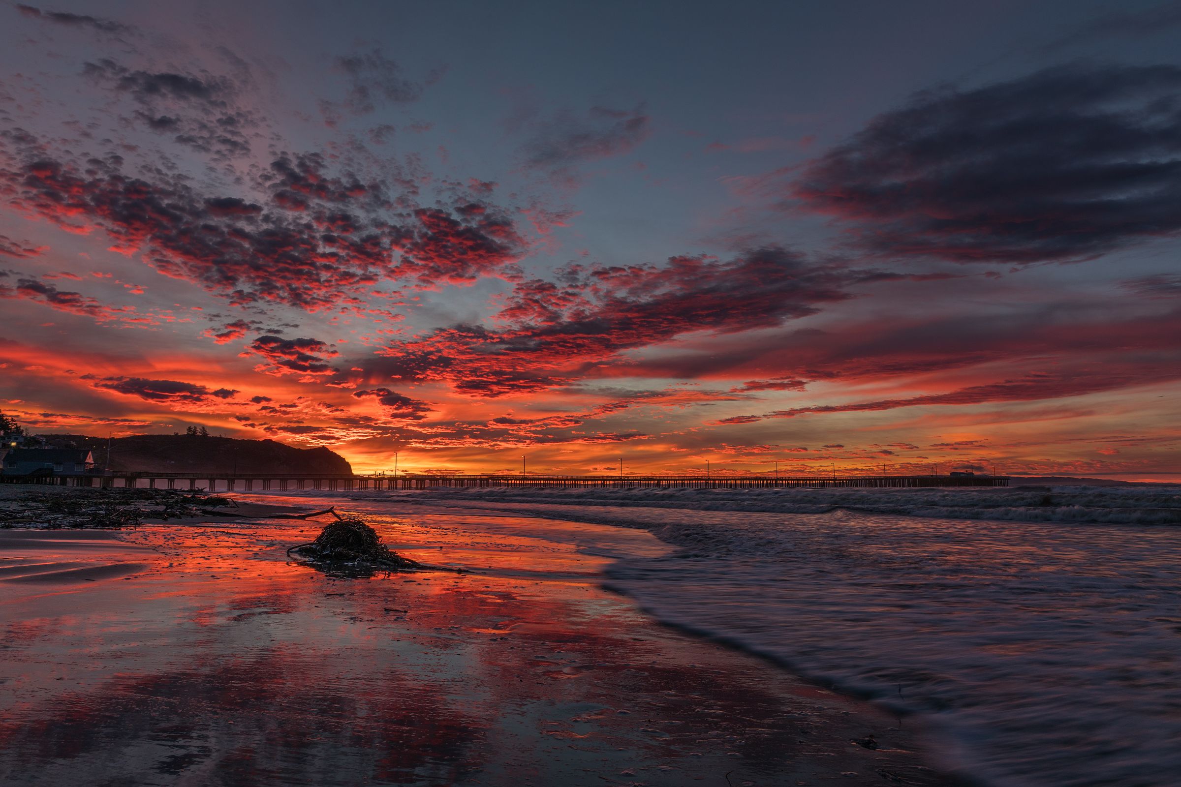 Red sunrise sky reflected on wet sand below Avila Pier