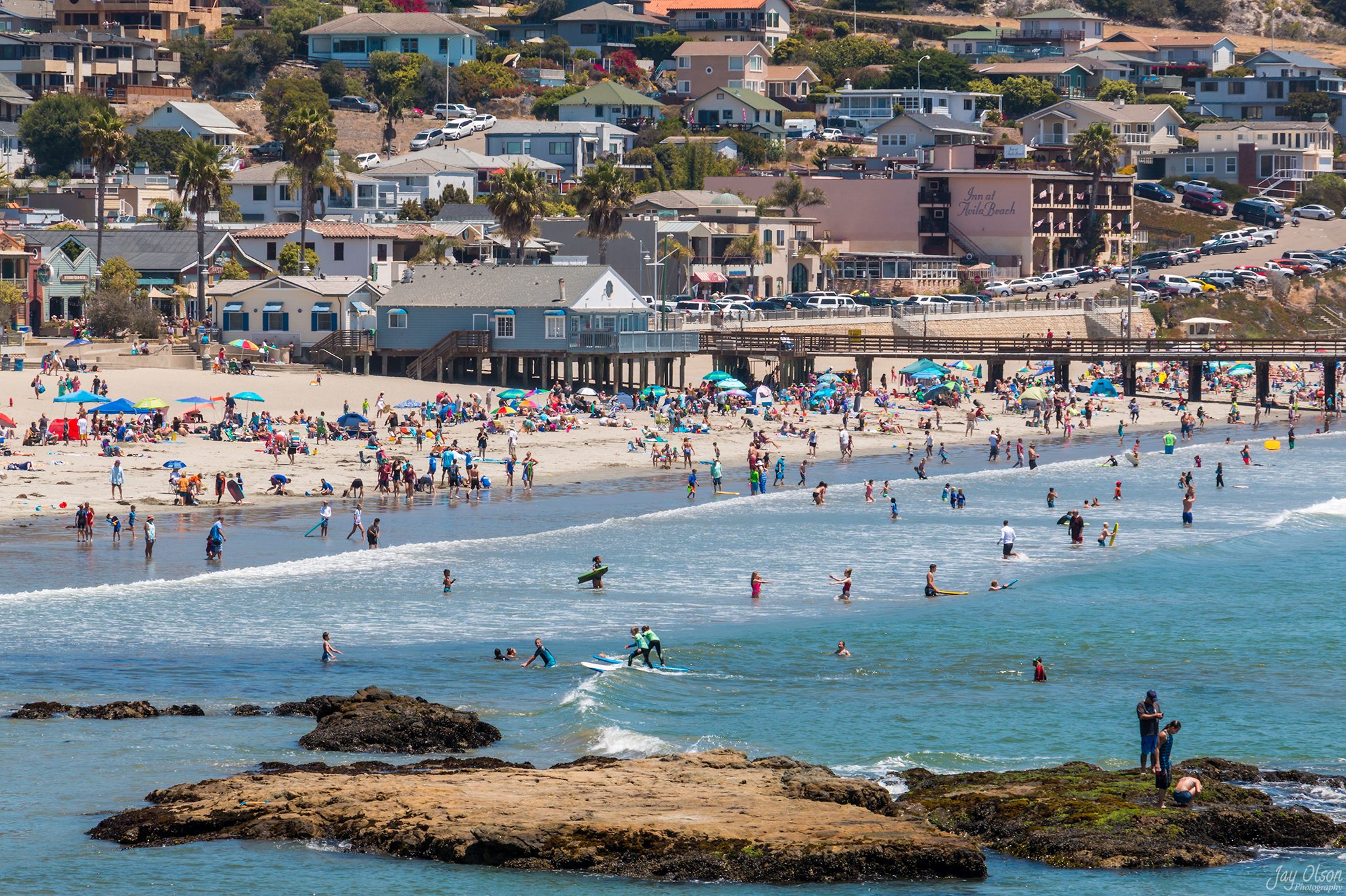 A crowded summer day on Avila Beach, with swimmers, bodyboards and a surf lesson in the water