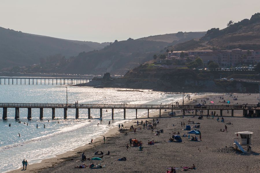 Beachgoers on Avila Beach in hazy late-day light, with Avila Pier and Cal Poly Pier behind