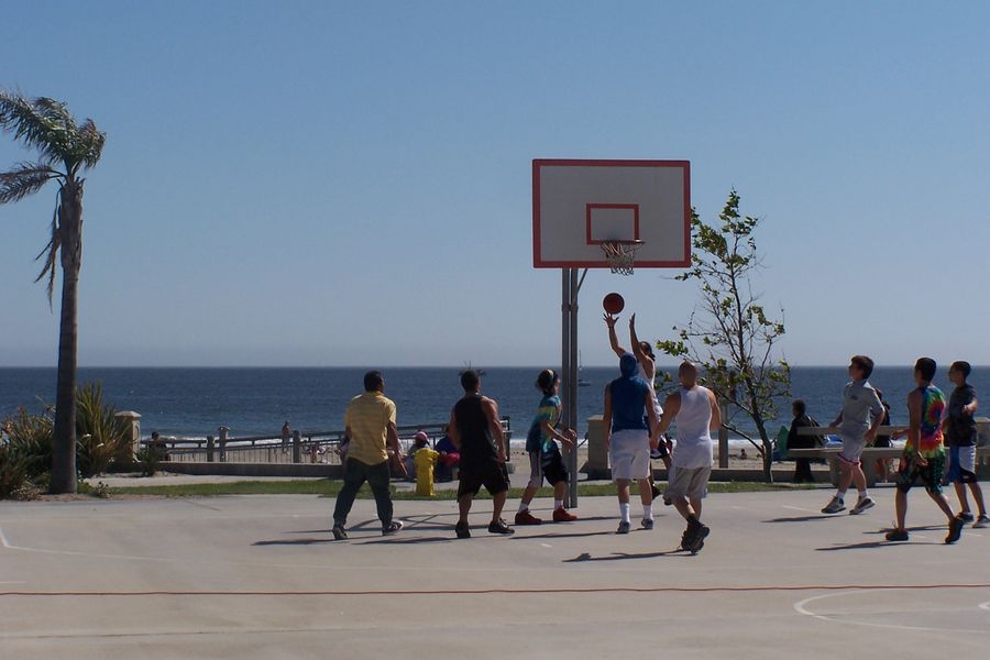 A pickup basketball game on the court at Avila Beach Park, with the beach and the ocean right behind