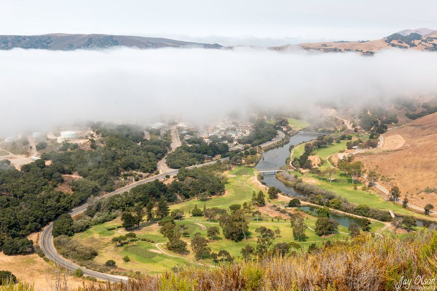 Fog rolling over Avila Beach seen from a hilltop, with the golf course, San Luis Obispo Creek and Avila Beach Drive below