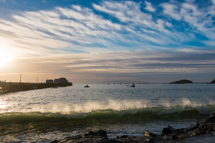 A wave breaking near Harford Pier under streaky clouds, with Whaler's Island in the distance