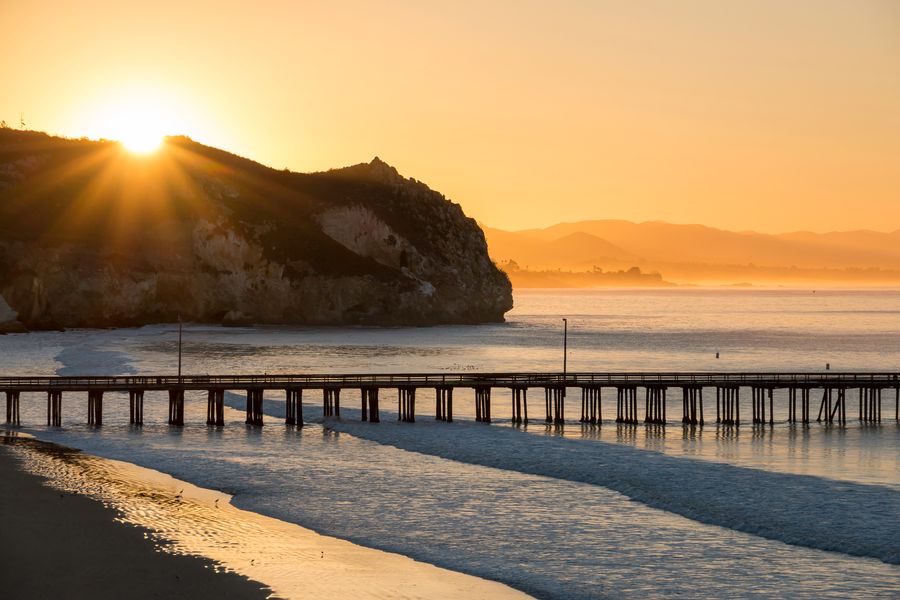 The sun rising over the headland behind Avila Pier, with the coast fading into gold
