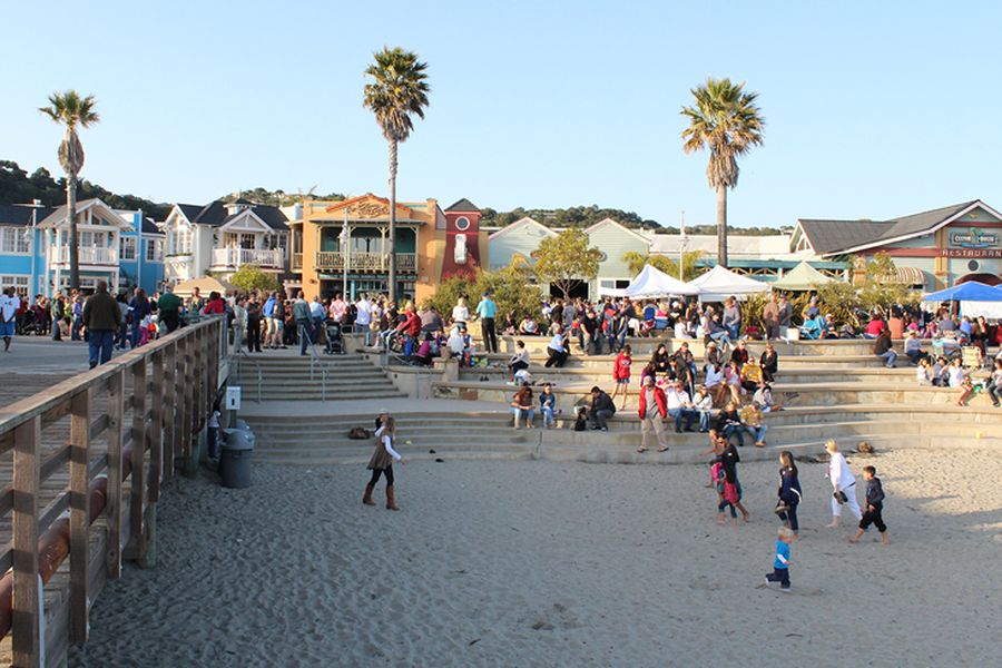 Friday farmers market crowds on the beach steps and sand below Front Street, with white tents and palms