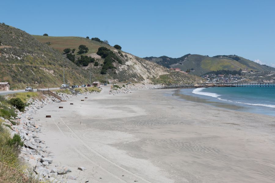 The long sandy stretch of Olde Port Beach below the hills, with fire rings, the parking pullouts along the road and Avila Pier in the distance