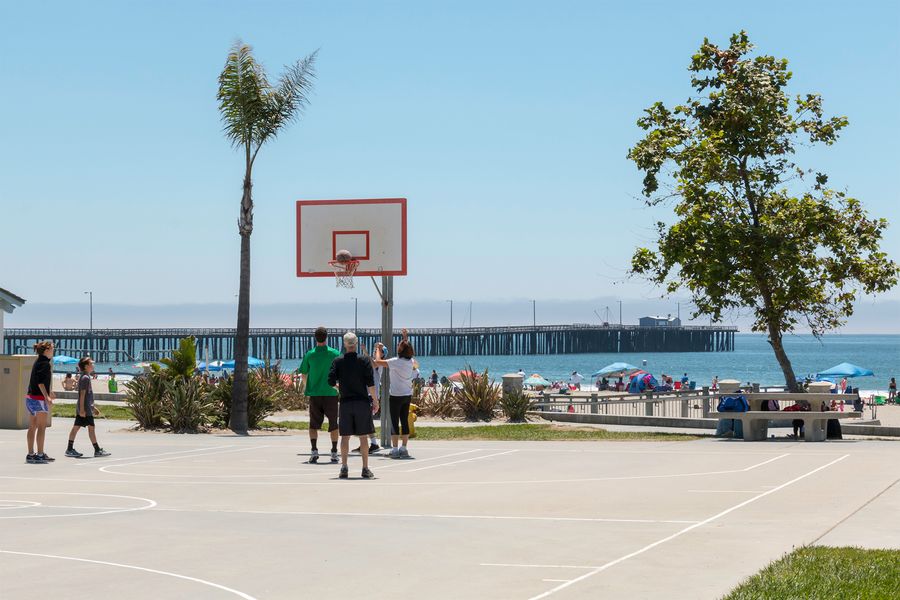 A pickup basketball game at Avila Beach Park, with the beach and pier behind