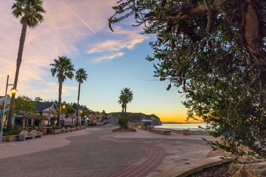 Street lamps glowing along the Front Street promenade at dusk, with the beach and headland ahead