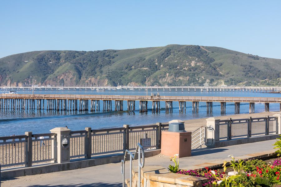 The promenade railing above the beach, with Avila Pier, Cal Poly Pier and green spring hills behind