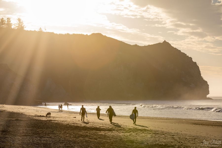 Surfers carrying their boards up Avila Beach in golden morning light below the headland