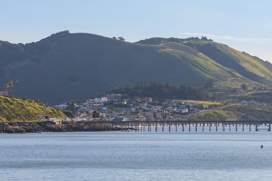 The houses of Avila Beach on the hill above the beach, seen across the bay with green hills behind